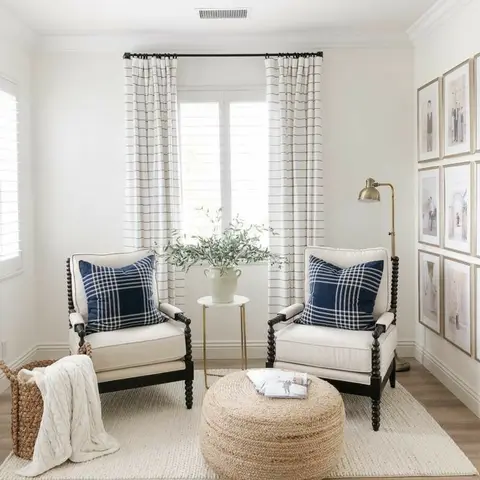 Reading nook with two black spindle-leg armchairs in navy plaid pillows, a jute pouf, and a gallery wall of framed photos.