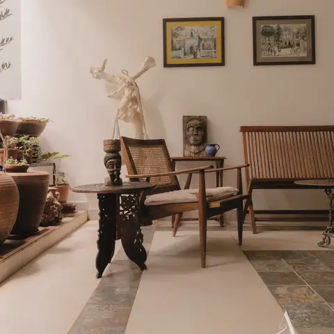 Real eclectic sitting nook with a cane-back wooden armchair, a slatted wood bench, a carved antique side table topped with a sculptural bust