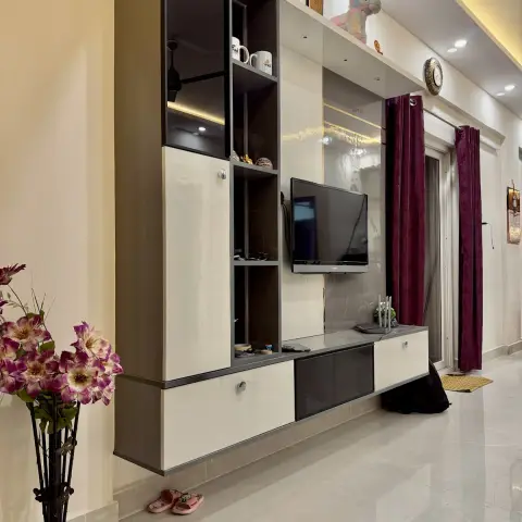 Real living room with a floor-to-ceiling glossy grey-and-white TV unit with open display shelving, a wall-mounted TV, maroon patterned curtains