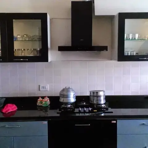 Real modular kitchen with black granite countertops, dark grey shutters, glass-front upper display cabinets, a black chimney hood