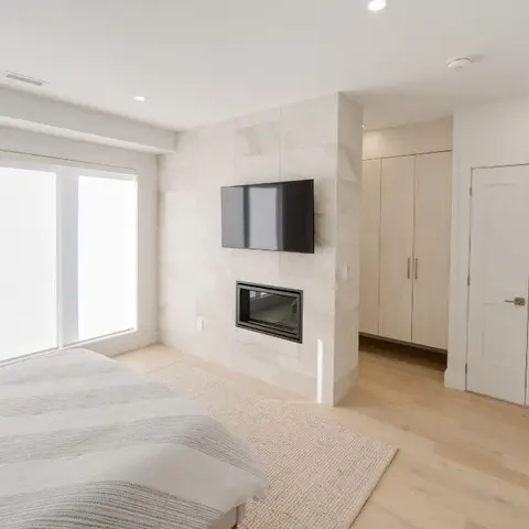 Real photo of a bedroom with a floor-to-ceiling stone-tiled fireplace wall with a wall-mounted TV above it, light oak flooring