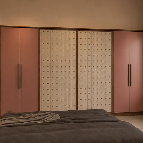 Real photo of a bedroom with a terracotta-pink wardrobe featuring a cream palm-print fabric center panel, a wood-trimmed window seat with sheer curtains
