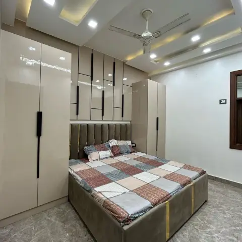 Real photo of a bedroom with a grey velvet channel-tufted headboard trimmed in gold, flanking beige glossy wardrobes with vertical black-strip inlays