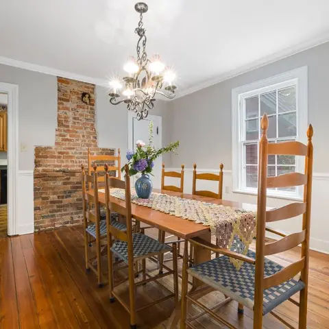Real photo of a farmhouse-style dining room with an exposed brick chimney breast, a wrought-iron candle chandelier, wide-plank wood flooring