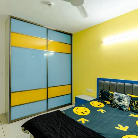 Real photo of a kids' bedroom with a bright yellow accent wall, a blue-and-yellow colour-blocked sliding wardrobe
