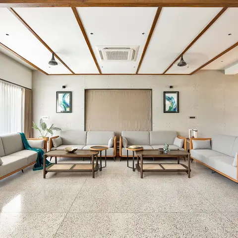 Real photo of a living room with speckled terrazzo flooring, an exposed concrete-panelled feature wall, a wood-beamed ceiling