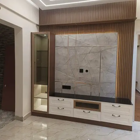 Real photo of a living room TV wall with fluted wood panelling framing a brass-inlaid grey marble slab, a glass-front display cabinet