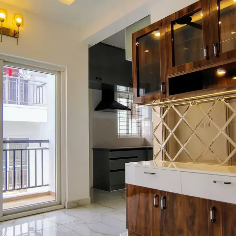 Real photo of a wood-grain crockery unit with a brass diamond-mesh backsplash beside a balcony sliding door