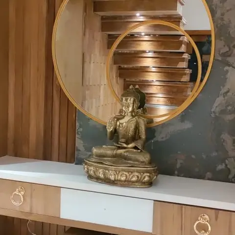 Real photo of an entrance console styled with a brass seated Buddha statue beneath overlapping circular gold-framed mirrors