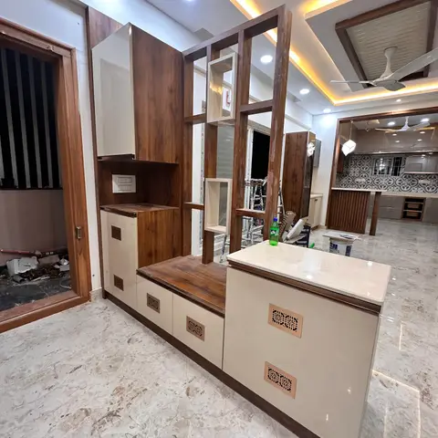 Real photo of an entrance foyer under construction with a wood jaali-style partition screen and shoe/storage console in walnut and cream finishes