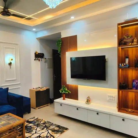 Real photo of an Indian living room with a navy velvet sofa, a white-and-walnut TV unit with backlit fluted wood accent panel and open display shelving