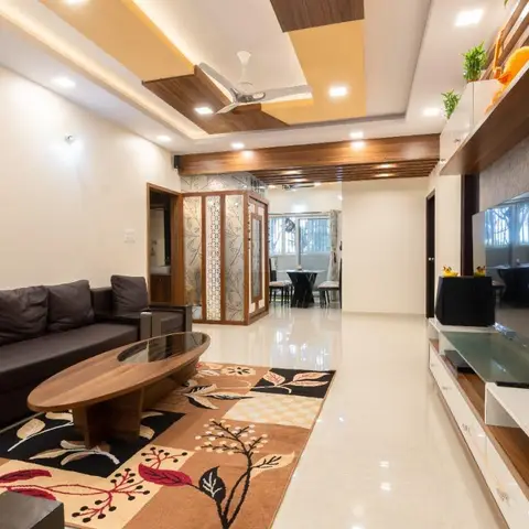 Real photo of an open living-dining apartment with a stepped wood-and-POP false ceiling, a jaali-screened pooja nook off the hallway