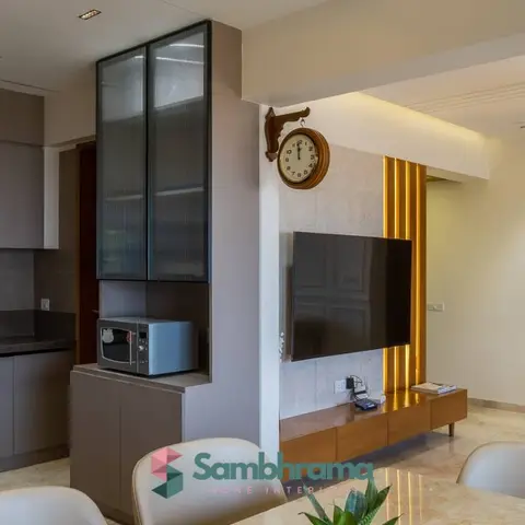 Real photo of an open-plan kitchen and living area with a grey handleless kitchen run, a stone-clad TV wall with vertical brass fluting