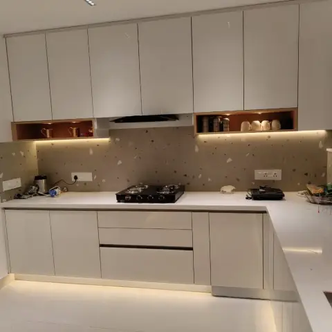 Real U-shaped kitchen with matte off-white cabinetry, a speckled terrazzo-effect backsplash, open wood-lined display niches for mugs, and toe-kick LED lighting.