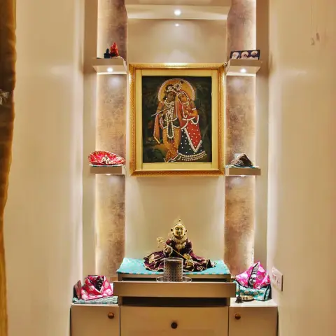 Recessed pooja niche with a gold-framed beaded Radha-Krishna picture between two mottled-metallic half-column returns
