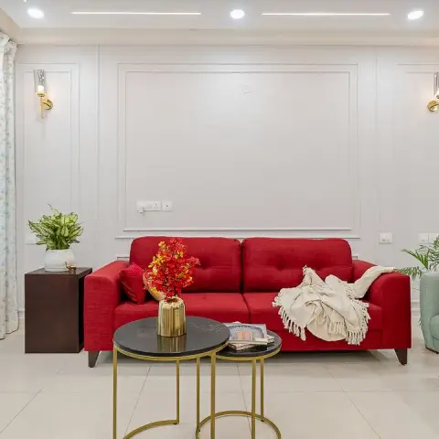 Red fabric three-seater set against a white moulded panel wall flanked by brass cylinder sconces, with nesting black-marble-top brass tables on ivory tiles.