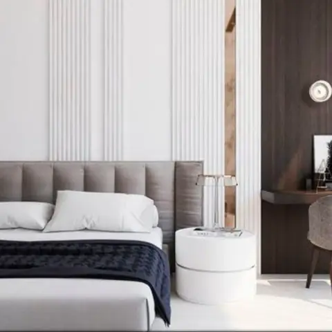 Render of a bedroom where a wide grey upholstered headboard runs across a white fluted wall panel, a round drum bedside table sits beside it