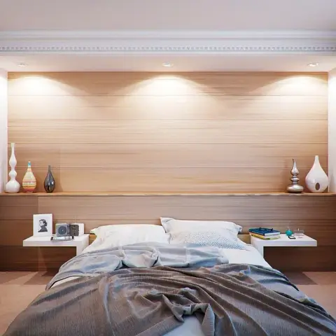 Render of a bedroom with a horizontal wood-veneer headboard wall lit by four ceiling washers, a continuous ledge carrying vases across it