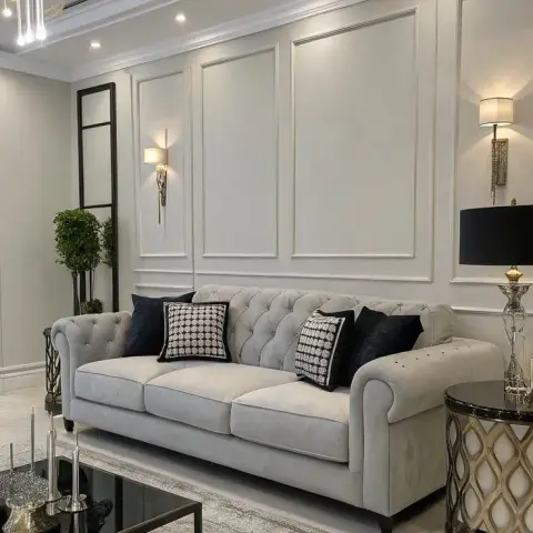 Render of a grey-and-white living room where a buttoned grey chesterfield sits against moulded wall panels lit by two brass sconces