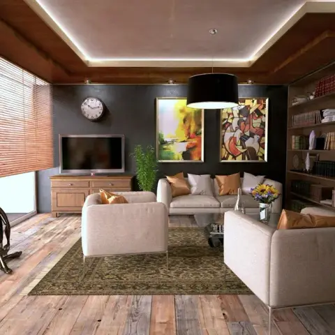 Render of a living room with two abstract canvases and a round wall clock on a charcoal wall, beige sofa and armchairs on a faded Persian rug