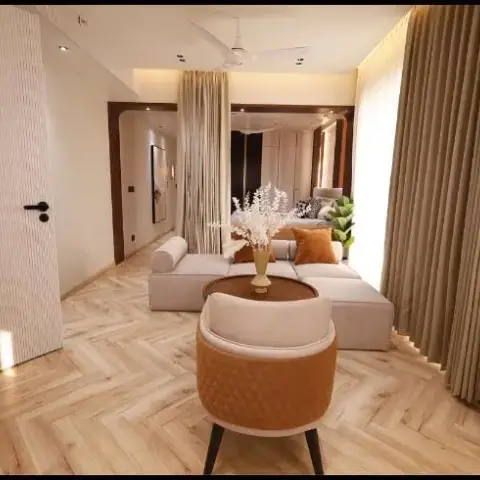 Render of a narrow beige living room — low modular sofa and a tan quilted tub chair around a round wood table on chevron-laid light wood flooring