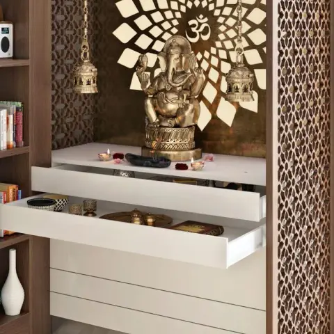 Render of a pooja unit with a gold Om sunburst backdrop, a Ganesha idol, jaali side panelling and white pull-out drawer storage below.