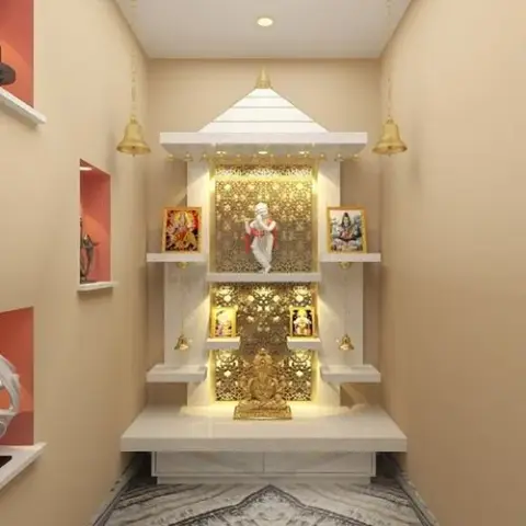 Render of a wall-niche pooja unit with a white stepped canopy, gold jaali backdrop panels and hanging bells flanking a marble platform