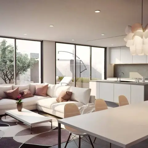 Render of an open-plan floor where a white L-sofa with dusty-rose cushions, a long white dining table and a handleless island kitchen share one room