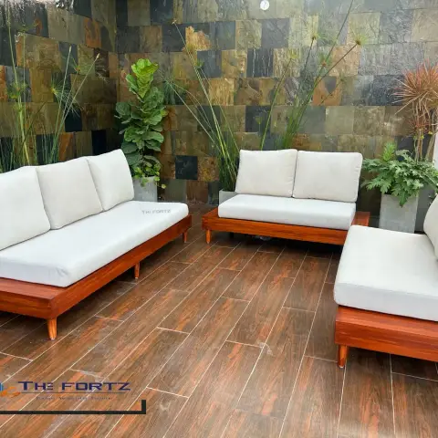 Rooftop balcony seating area with three wood-framed cushioned sofas arranged around a slate-tile accent wall and potted ornamental grasses