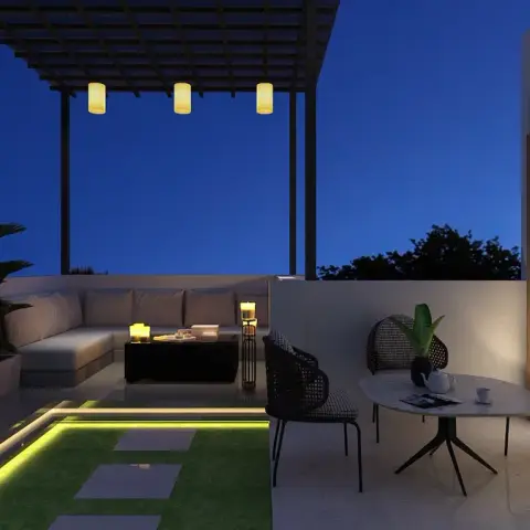 Rooftop terrace at dusk where a steel pergola carries three cylinder lanterns over a built-in L-banquette