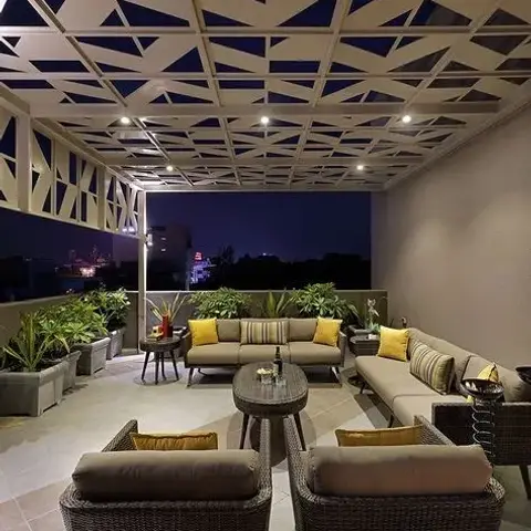 Rooftop terrace lounge with a geometric triangular pergola ceiling, dark wicker sofas and armchairs with mustard cushions
