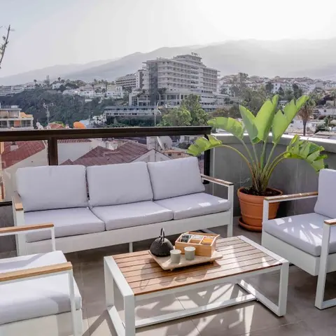 Rooftop terrace seating with a white outdoor sofa and armchairs around a wood coffee table, overlooking a hillside town view
