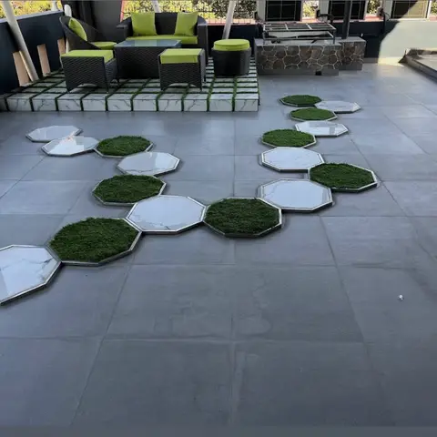 Rooftop terrace with a wicker outdoor sofa set with lime-green cushions, and a stepping-stone pathway alternating marble-look octagon pavers with synthetic