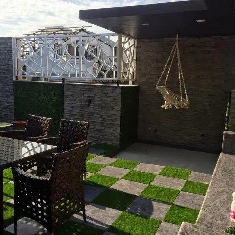 Rooftop terrace with checkerboard artificial-turf and stone paving, a stacked-stone accent wall, a decorative white jaali privacy screen