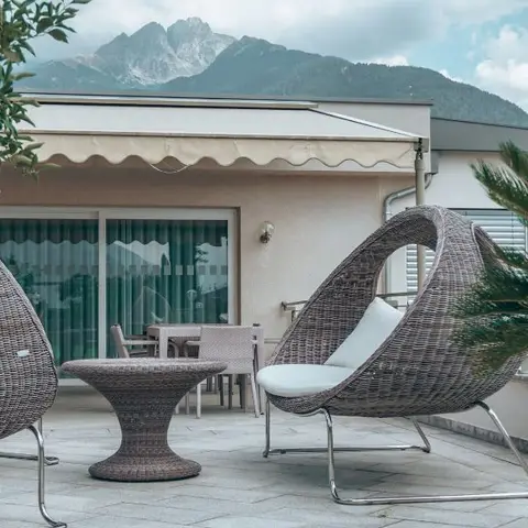 Rooftop terrace with woven pod-shaped lounge chairs and a matching side table, potted plants framing a mountain backdrop