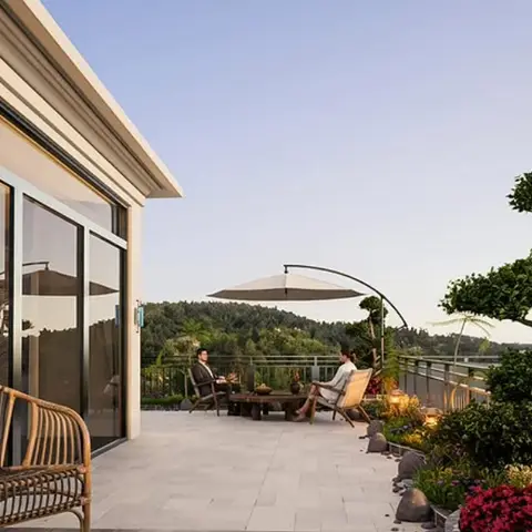 Rooftop terrace with woven rattan seating around a low table beneath a cantilever umbrella, framed by potted topiary and hillside views.