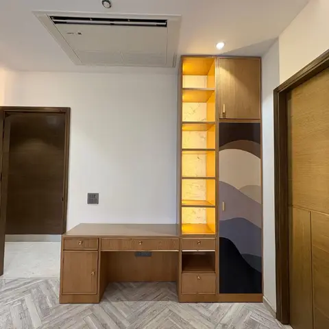 Room fit-out with a built-in study desk, open lit shelving and a wardrobe featuring a painted mountain-landscape door panel, over herringbone-pattern flooring.
