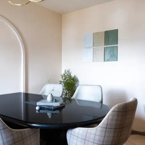 Round black lacquered dining table with mixed cream-leather and check-fabric chairs beneath a sculptural gold pendant