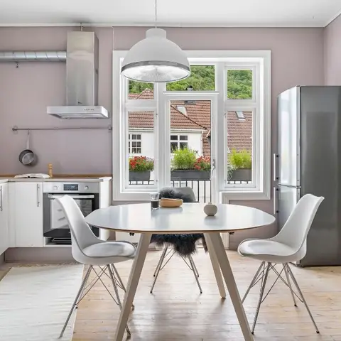 Round dining table with white shell chairs in a mauve-walled kitchen-dining space, beneath a large dome pendant.