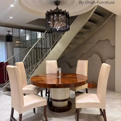 Round sunburst-veneer dining table with cream leather high-back chairs tucked under an open staircase