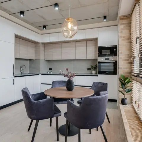 Round wood dining table with grey velvet chairs beneath an amber glass pendant light