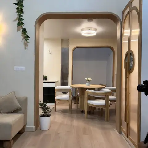 Rounded wood-lined archway framing a round fluted-base oak dining table with four cane-and-cream chairs, seen past a beige sofa