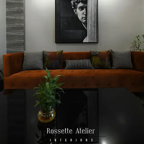Rust velvet tufted sofa styled with patterned cushions beneath a black-and-white classical portrait print, against a dark textured stone accent wall.