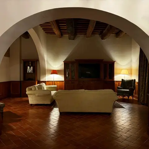 Rustic living room framed by a stone archway, with an exposed wood-beam ceiling, herringbone terracotta floor, cream slipcovered sofas