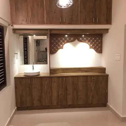 Rustic-oak laminate pooja unit with a CNC-carved arched jaali pelmet over a backlit white niche