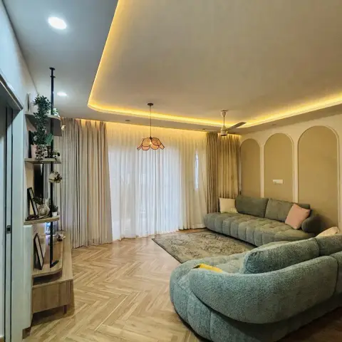Sage bouclé curved modular sofa on herringbone laminate, set against a beige wall of three tall arched mouldings with a scalloped rattan pendant over the
