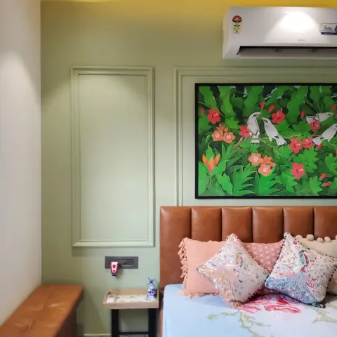 Sage-green bedroom wall picked out with slim applied mouldings, a Pichwai-style painting of mynahs among hibiscus hung over a tan channel-tufted leather