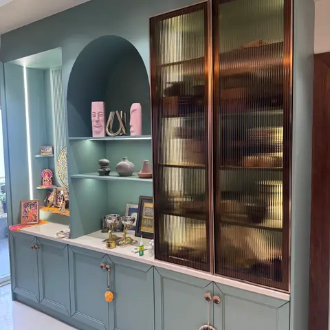 Sage-green display wall with an arched idol niche beside a bronze-framed fluted-glass crockery cabinet.