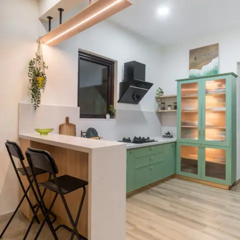 Sage-green L-kitchen with a terrazzo-topped breakfast peninsula, a ceiling-hung wooden shelf carrying an LED strip