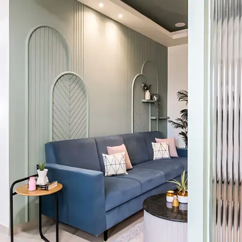 Sage-green living wall carved into three arched niches - two in chevron beading, one holding a small shelf - behind a slate-blue three-seater with blush